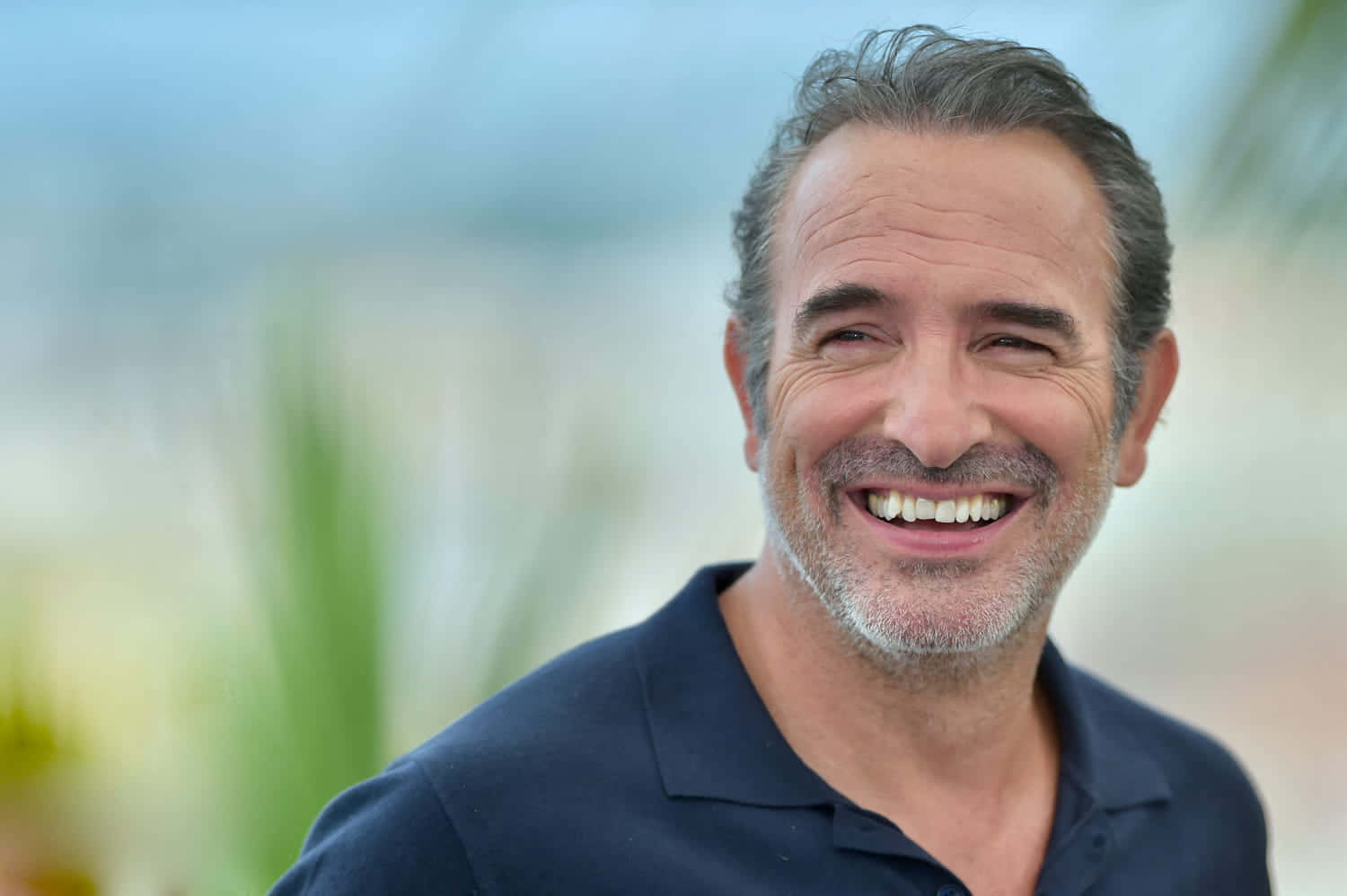 Jean Dujardin sonríe con fondo desenfocado.