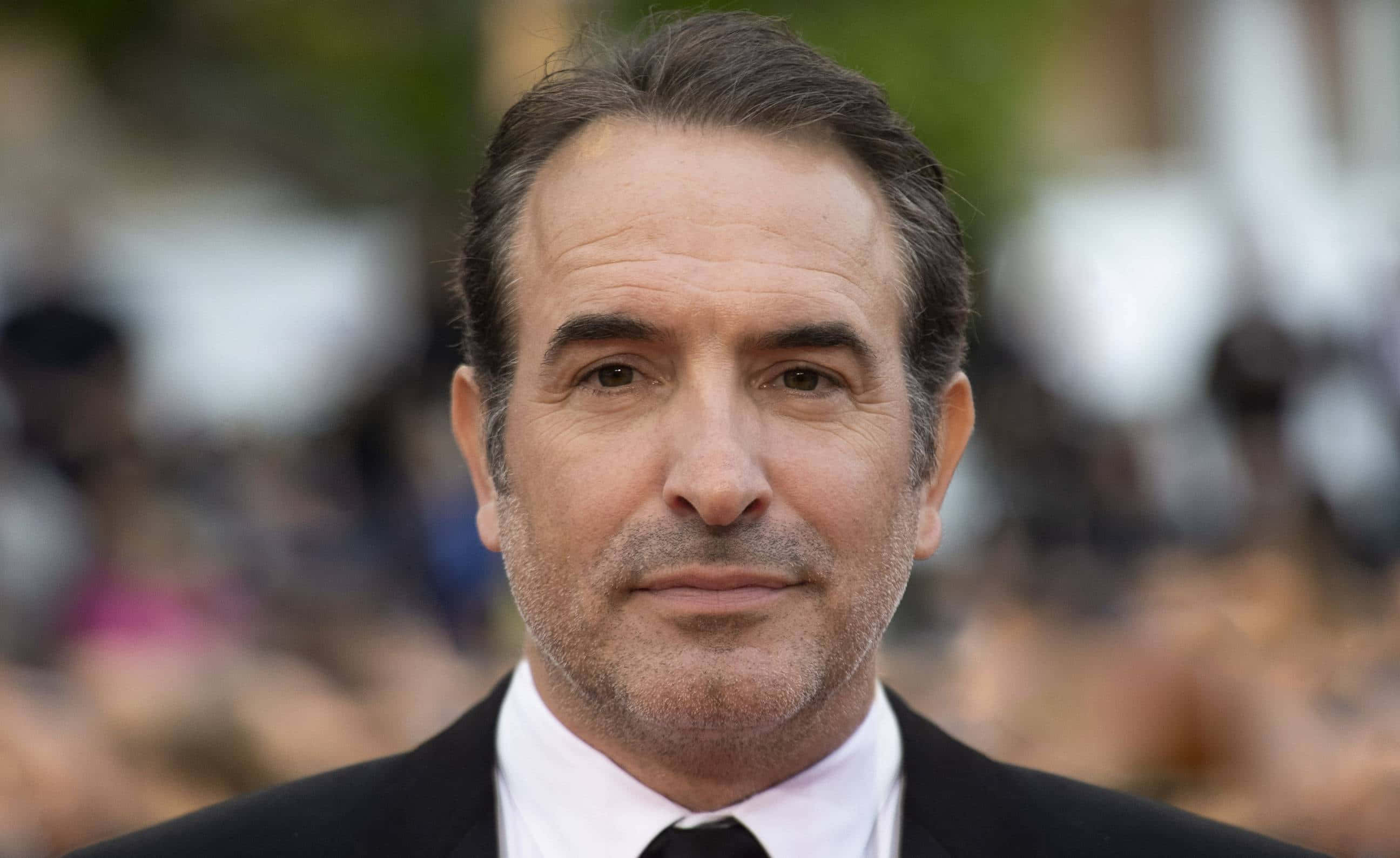 Actor Jean Dujardin en evento público con fondo borroso.