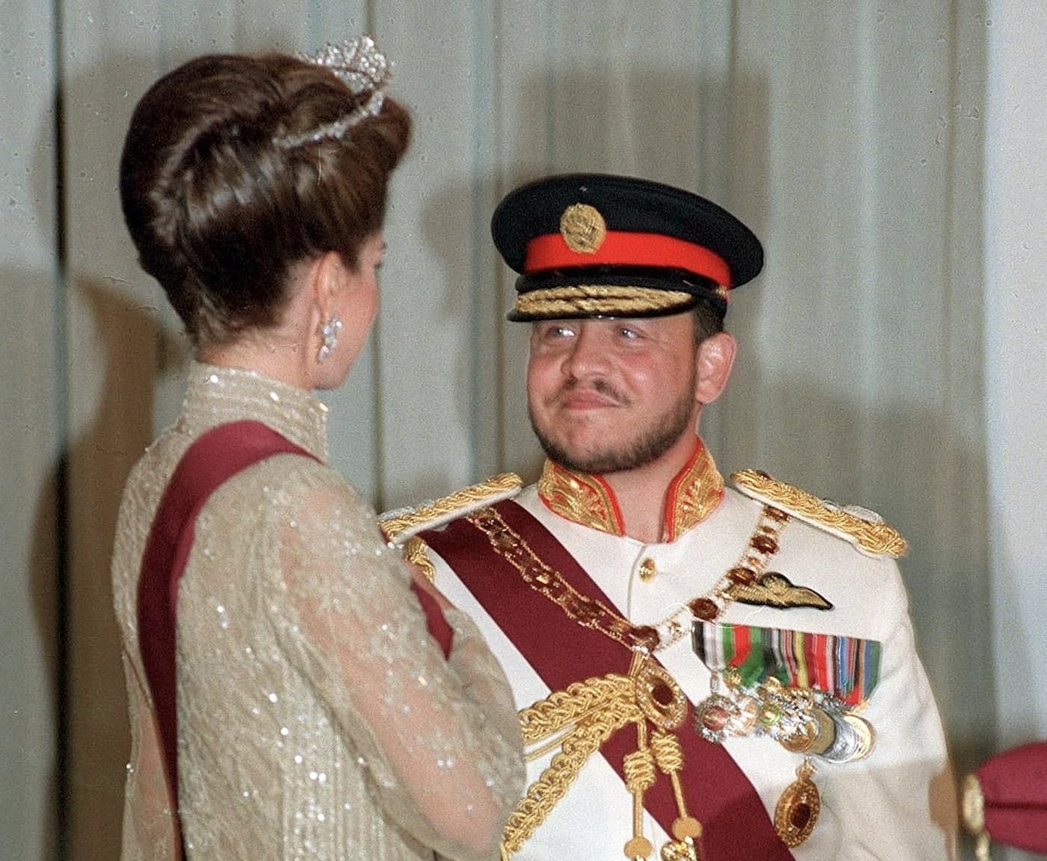 Rey Abdullah II con uniforme militar y decoración, sonriendo al interlocutor.