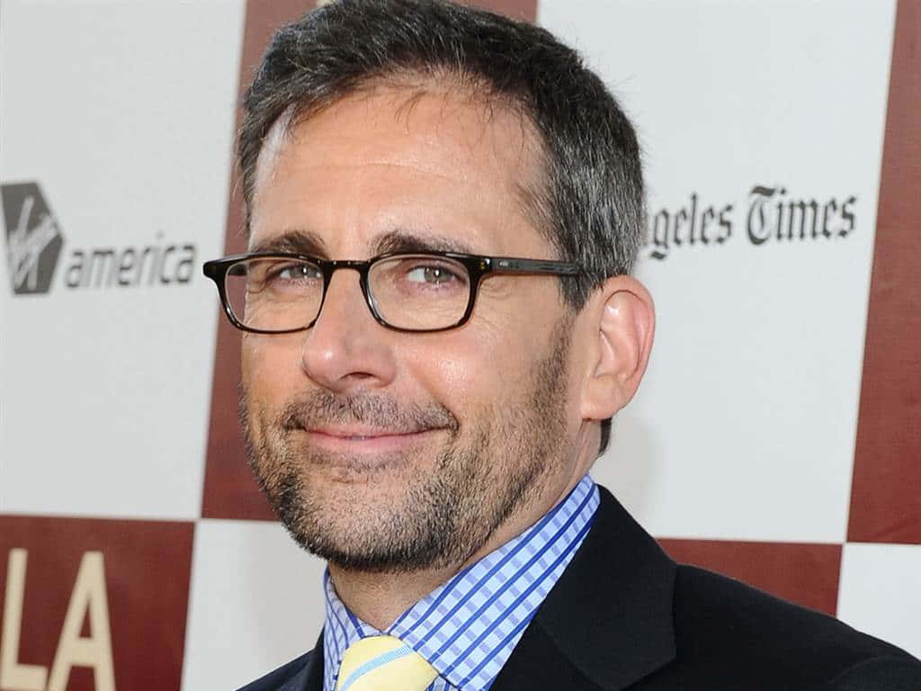Steve Carell sonriendo, con gafas y traje, fondo de evento.