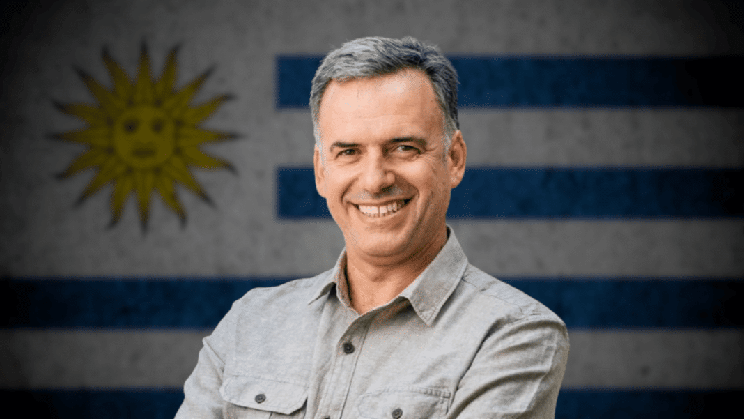 Yamandú Orsi sonríe con la bandera de Uruguay de fondo.